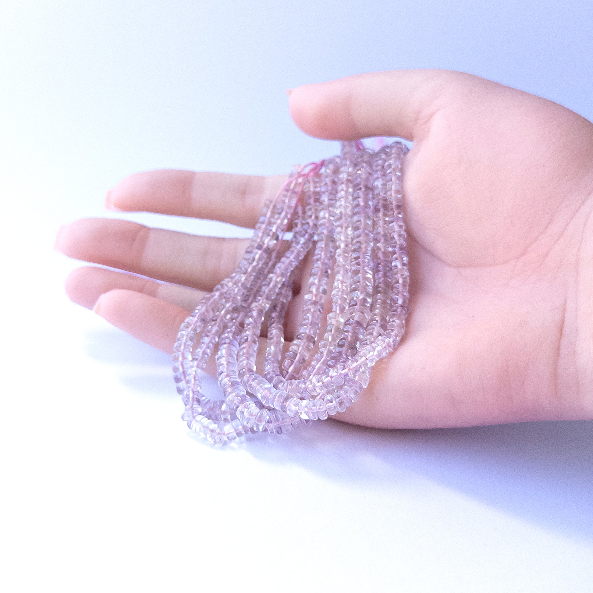 A person holds delicate strands of Pink Amethyst beads, showcasing their smooth wheel design.