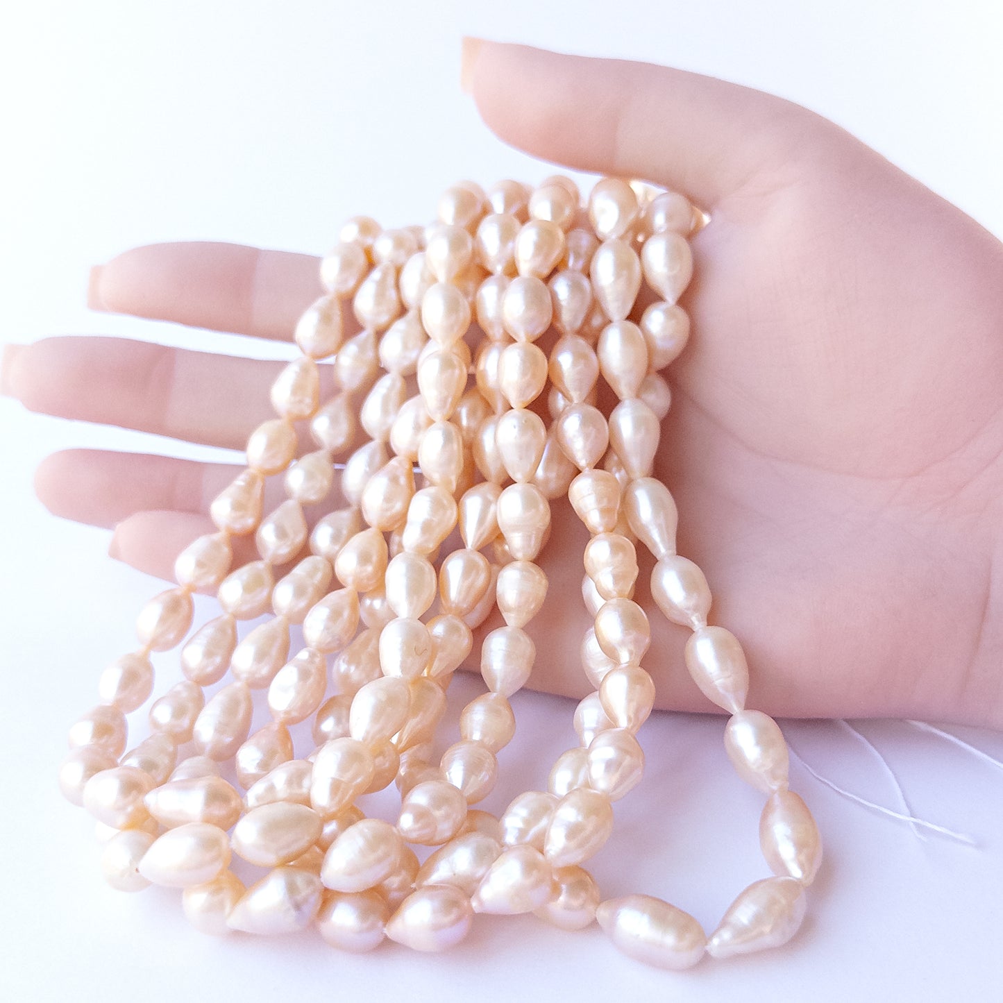 A person holds delicate strands of Pink Freshwater Pearls beads, showcasing their baroque oval design.