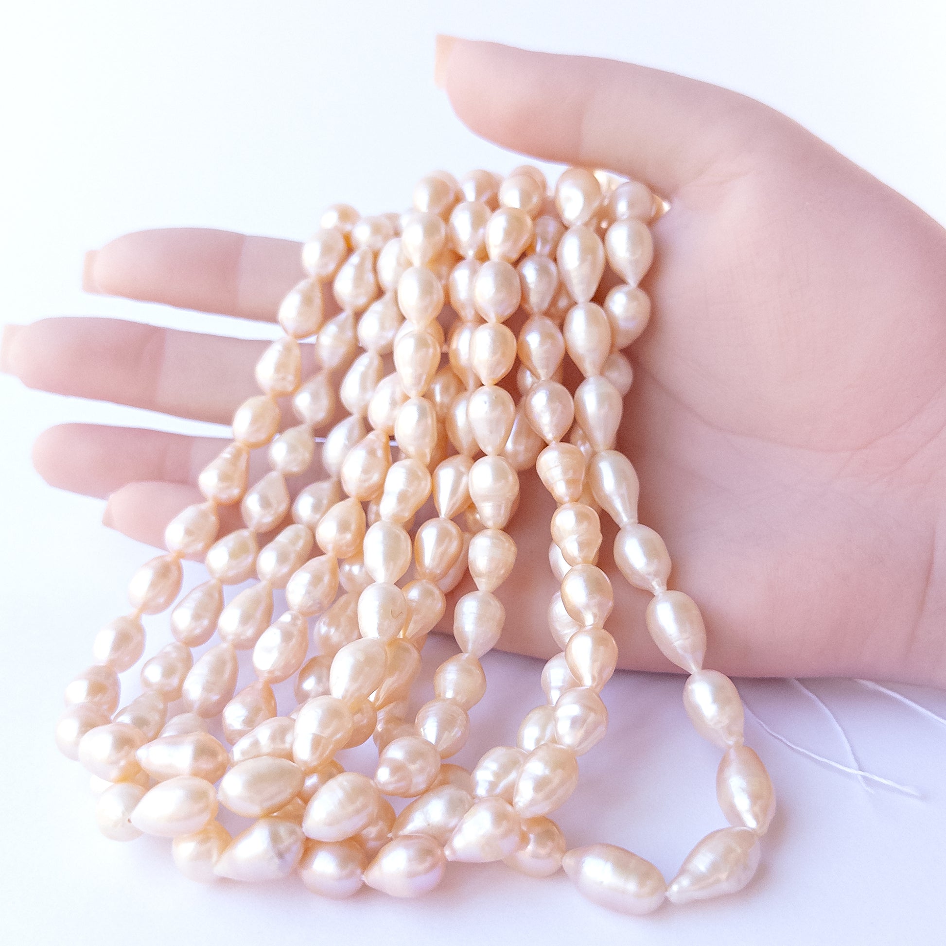 A person holds delicate strands of Pink Freshwater Pearls beads, showcasing their baroque oval design.