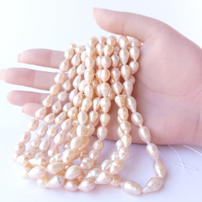 A person holds delicate strands of Pink Freshwater Pearls beads, showcasing their baroque oval design.