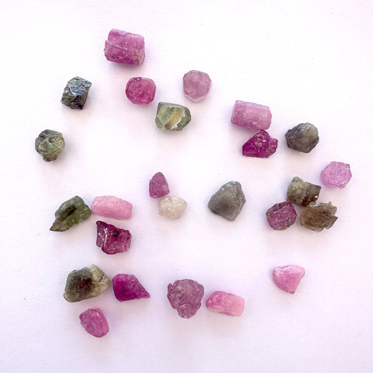 Close-up of undrilled pink and green sapphires showing raw edges and 8–11mm size range.