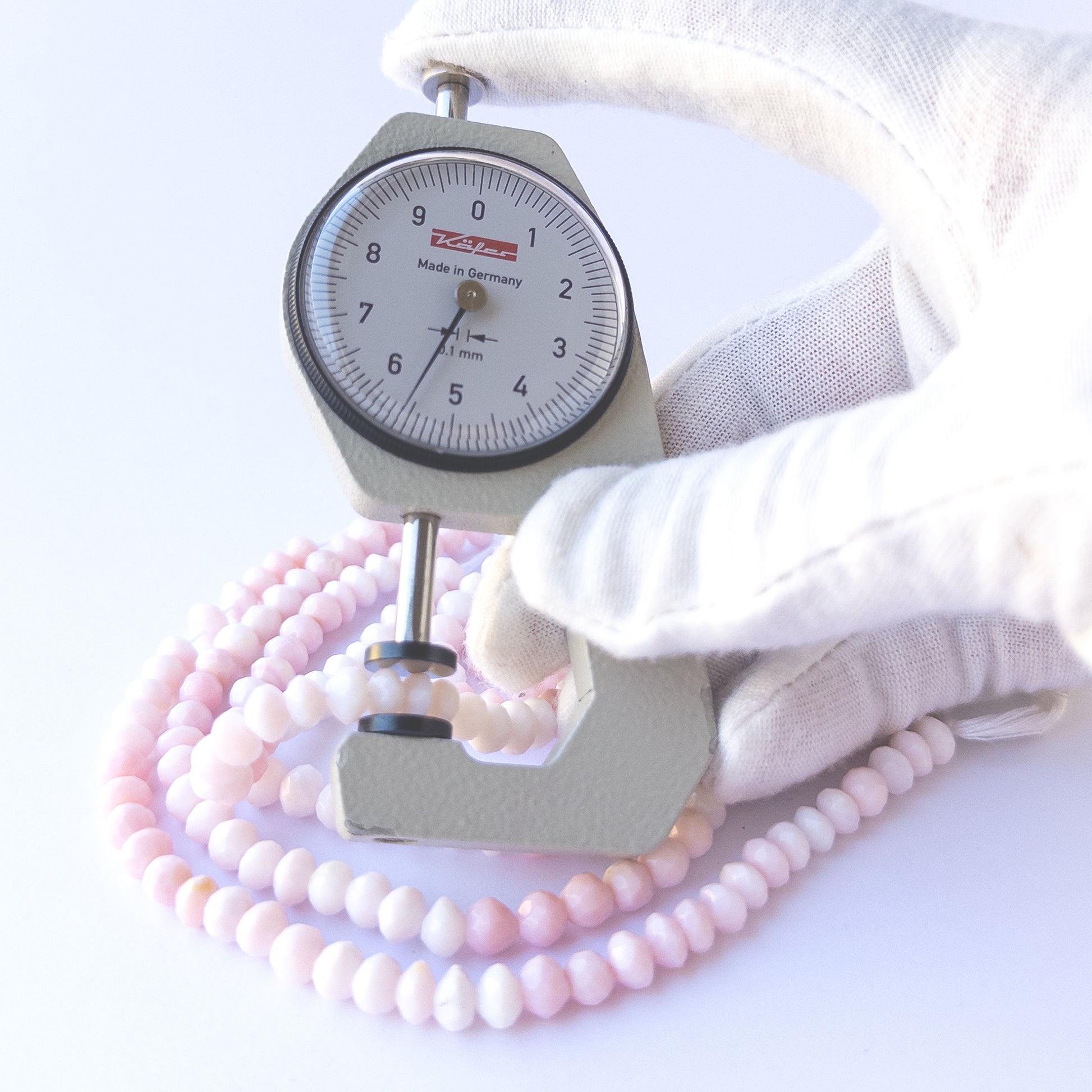 A dial gauge measures the Pink Opal faceted rondelle 5.5–6mm gemstone.