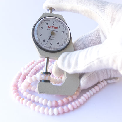 A dial gauge measures the Pink Opal faceted rondelle 5.5–6mm gemstone.