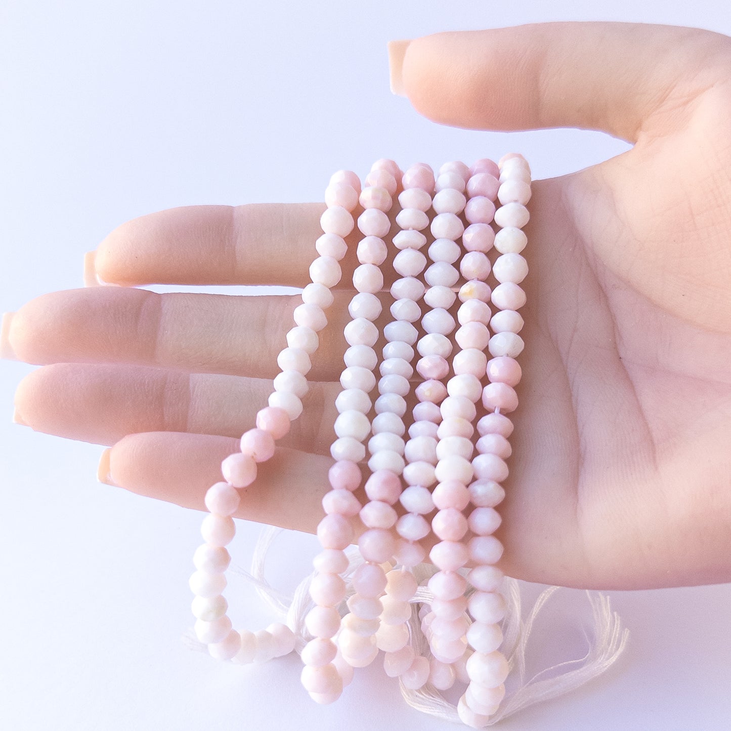 A person holds delicate strands of Pink Opal beads, showcasing their faceted rondelle design.