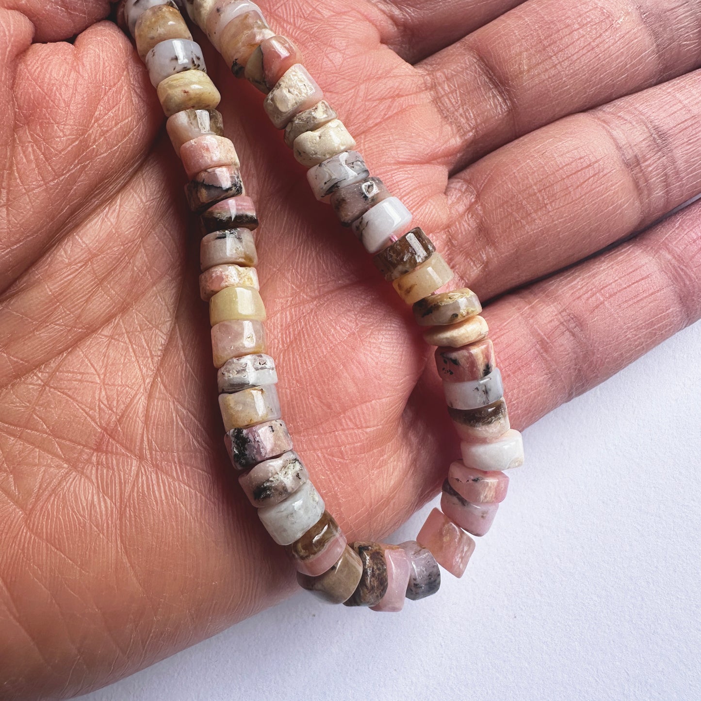 A person holds delicate strands of Pink Opal beads, showcasing their smooth design