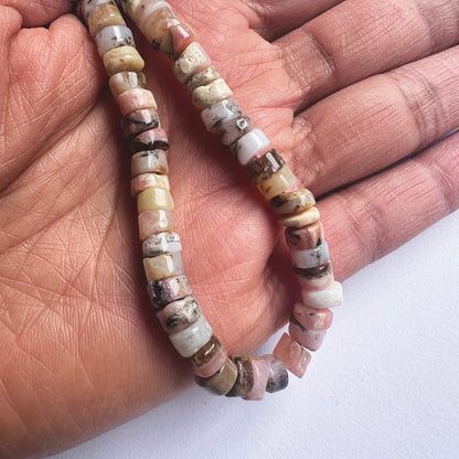 A person holds delicate strands of Pink Opal beads, showcasing their smooth design