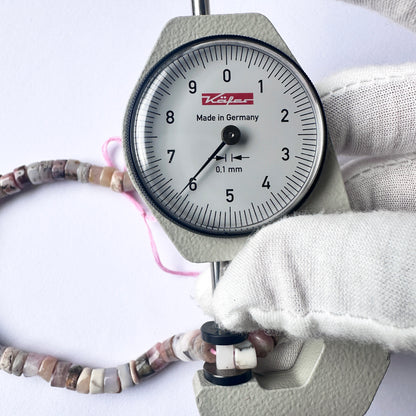 .A dial gauge measures the Pink Opal smooth disc gemstone.