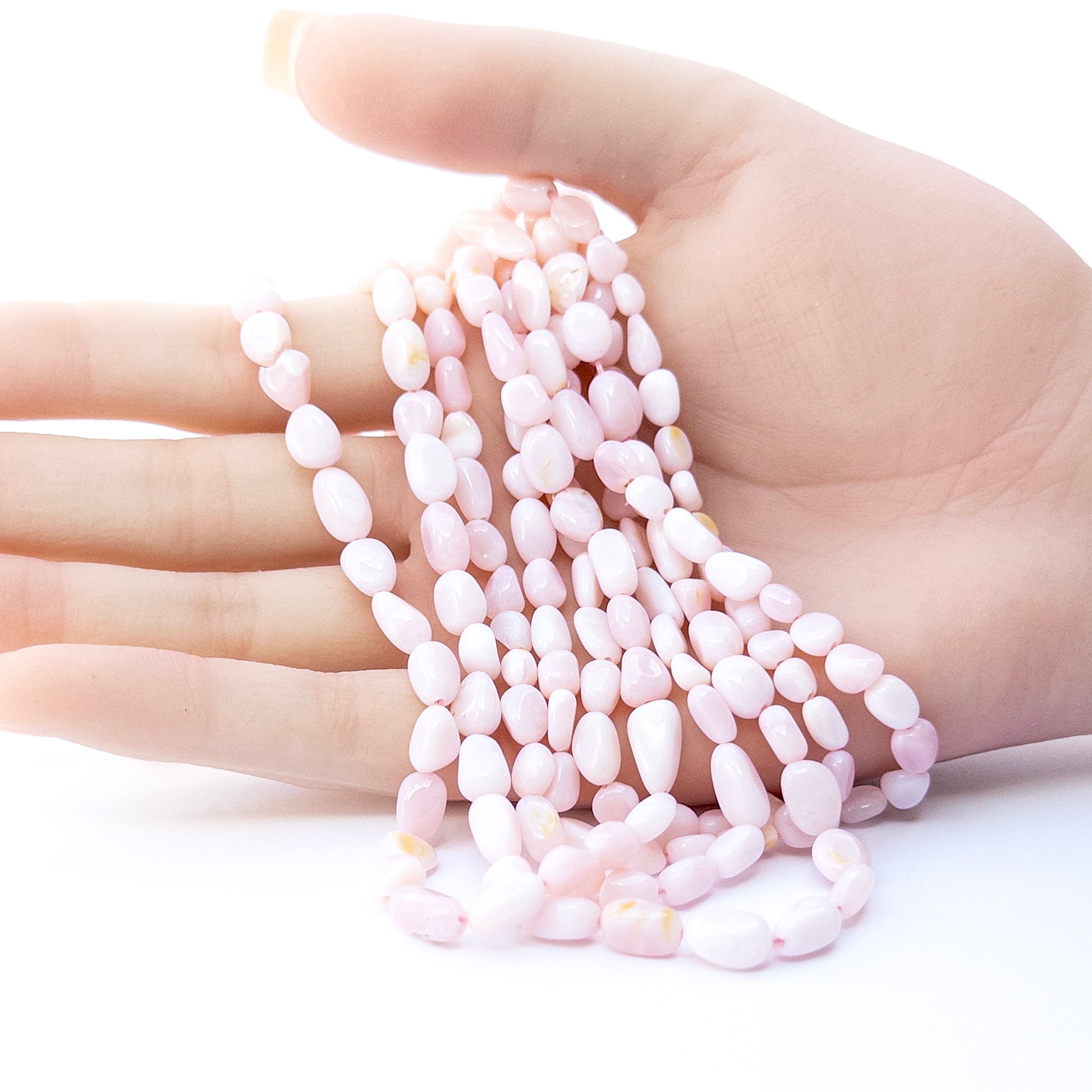 A person holds delicate strands of Pink Opal beads, showcasing their smooth tumble design.