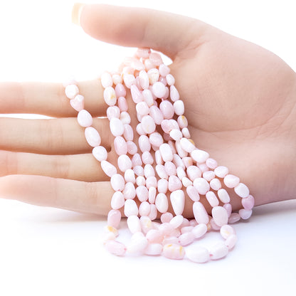 A person holds delicate strands of Pink Opal beads, showcasing their smooth tumble design.