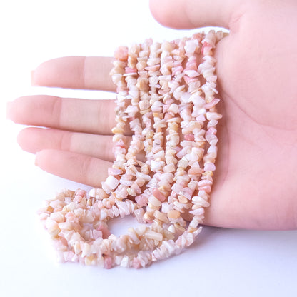 A person holds delicate strands of Pink Peruvian Opal chip beads, showcasing their natural chip design.