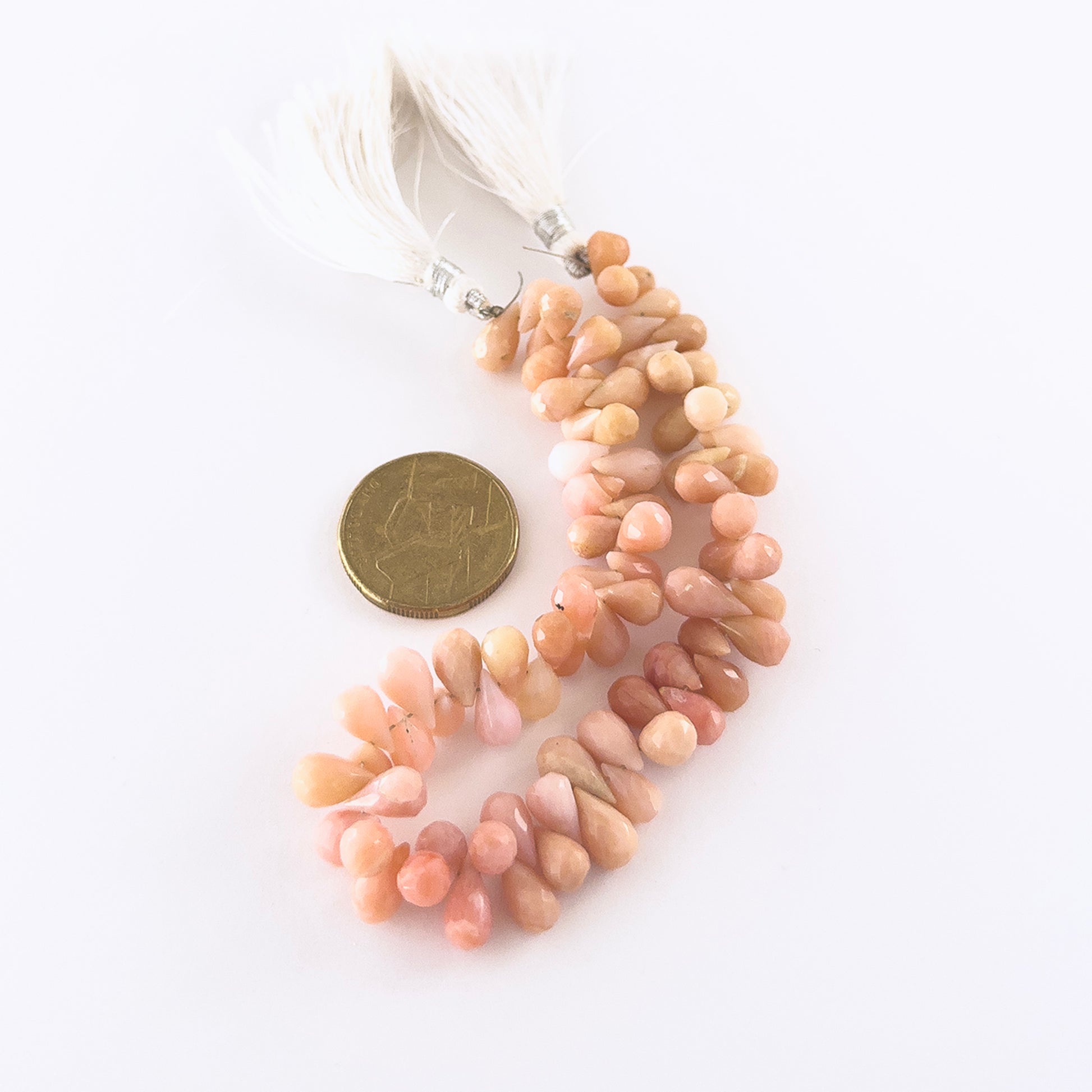 A coin is placed near Pink Peruvian Opal briolette beads to show the 6–6.5mm size range.