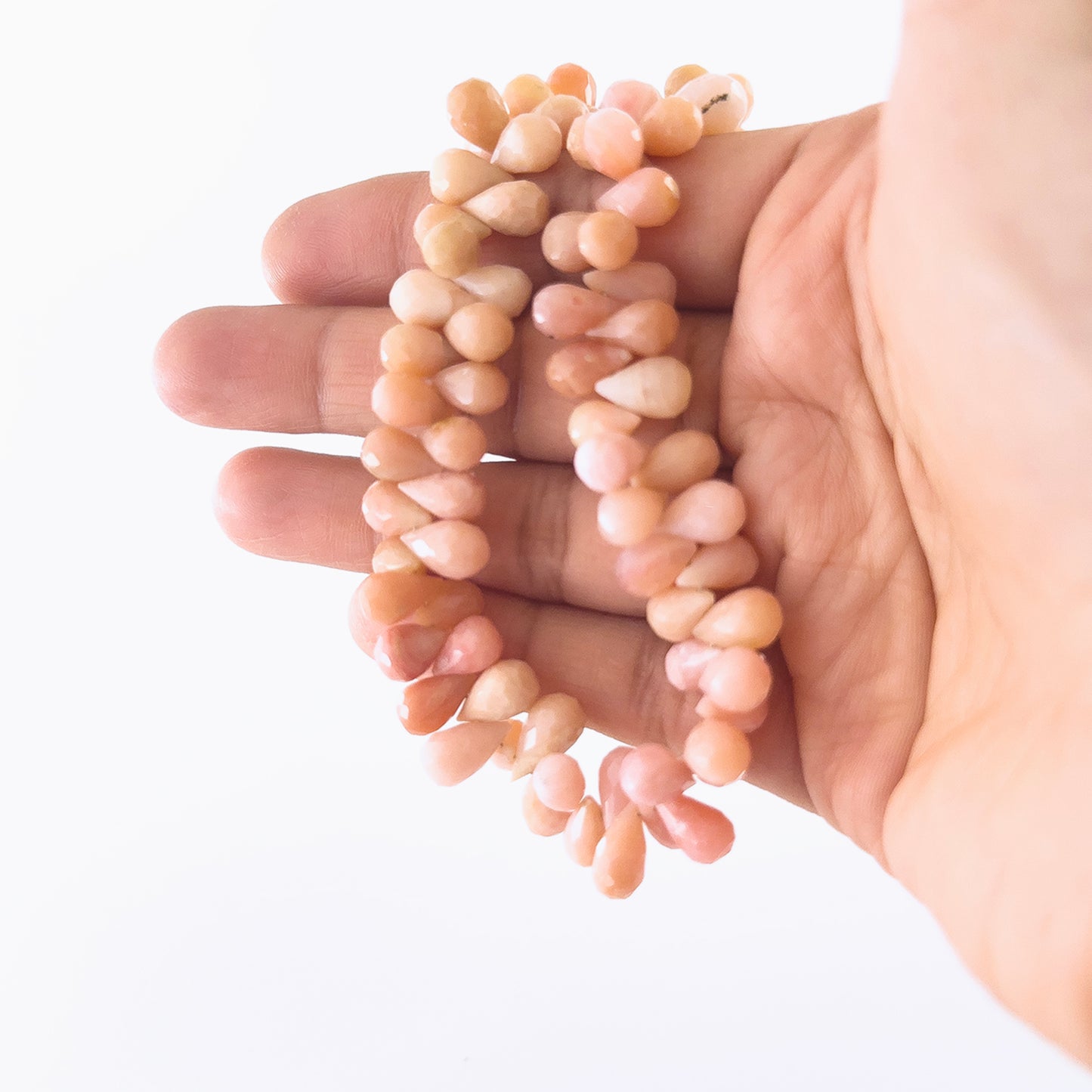 A person holds Pink Peruvian Opal briolette beads, showing their faceted teardrop design and pastel colour.