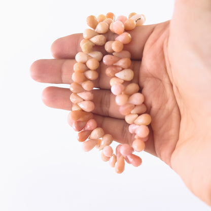 A person holds Pink Peruvian Opal briolette beads, showing their faceted teardrop design and pastel colour.
