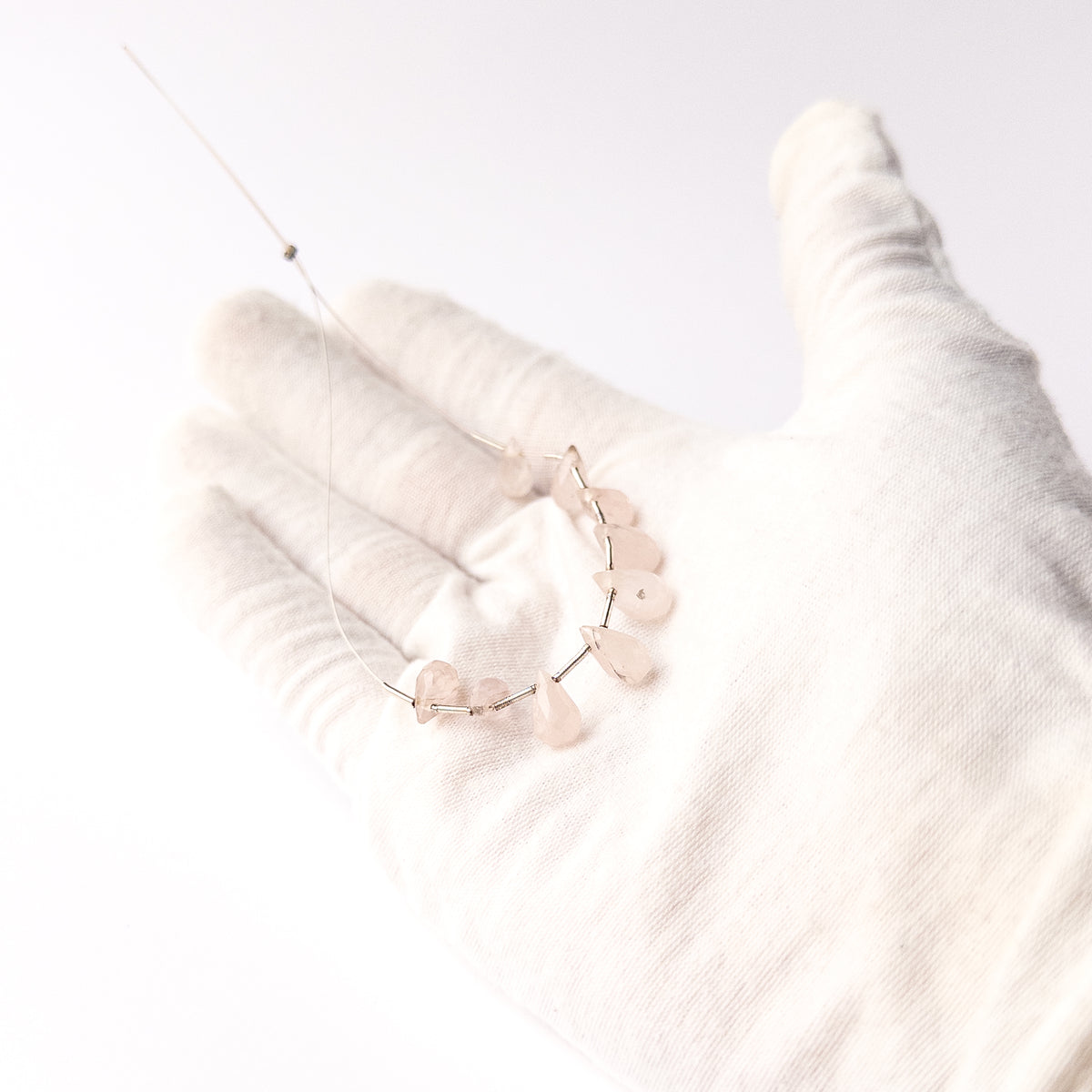 A person holds delicate pieces of Pink Quartz beads, showcasing their faceted briolette design.