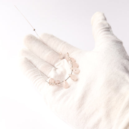A person holds delicate pieces of Pink Quartz beads, showcasing their faceted briolette design.