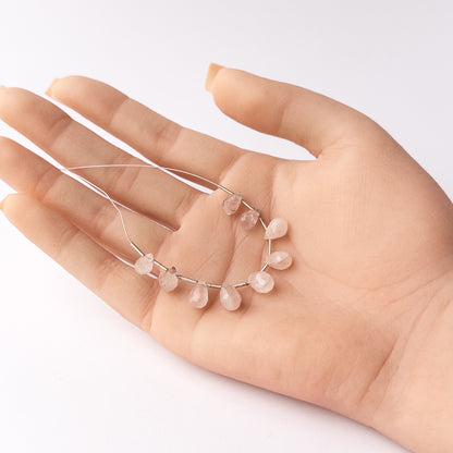 A person holds delicate pieces of Pink Quartz beads, showcasing their faceted briolette design.