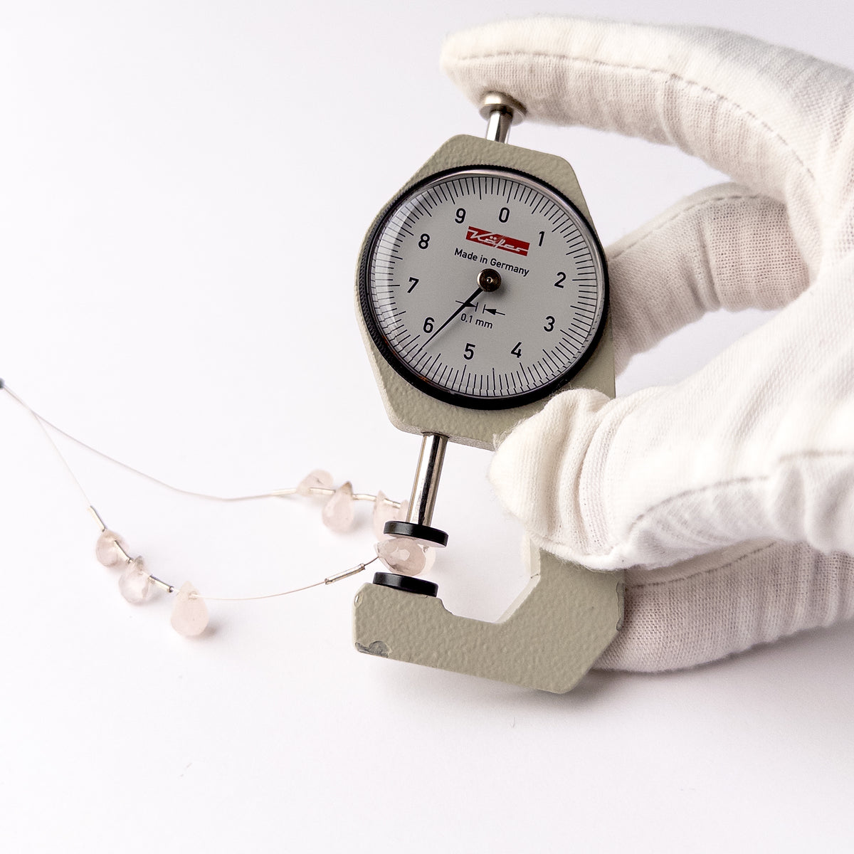 A dial gauge measures the Pink Quartz Faceted Briolette 5.5-6.5mm gemstone.