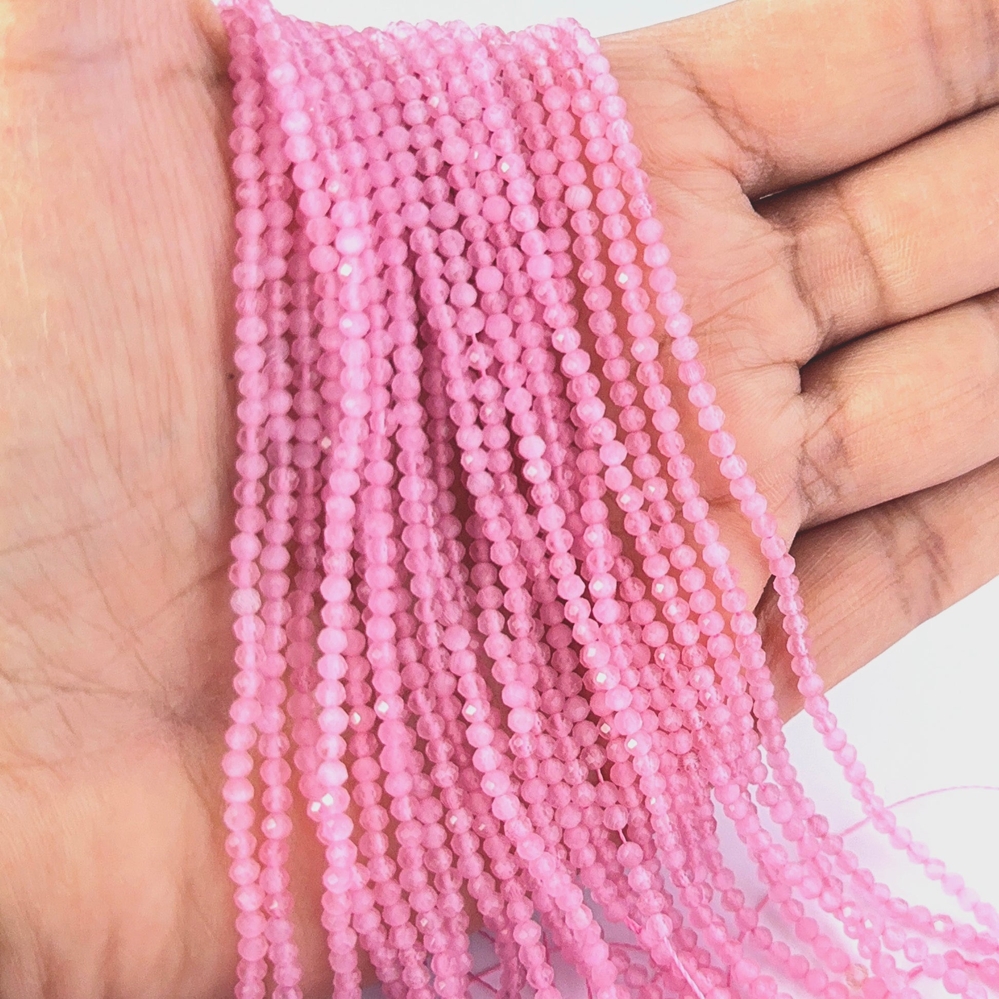 A person holds delicate strands of Pink Quartz beads, showcasing their faceted rondelle design