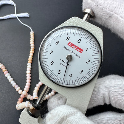 A dial gauge measures the Pink Shaded Opal faceted rondelle 4.2-4.5mm gemstone.