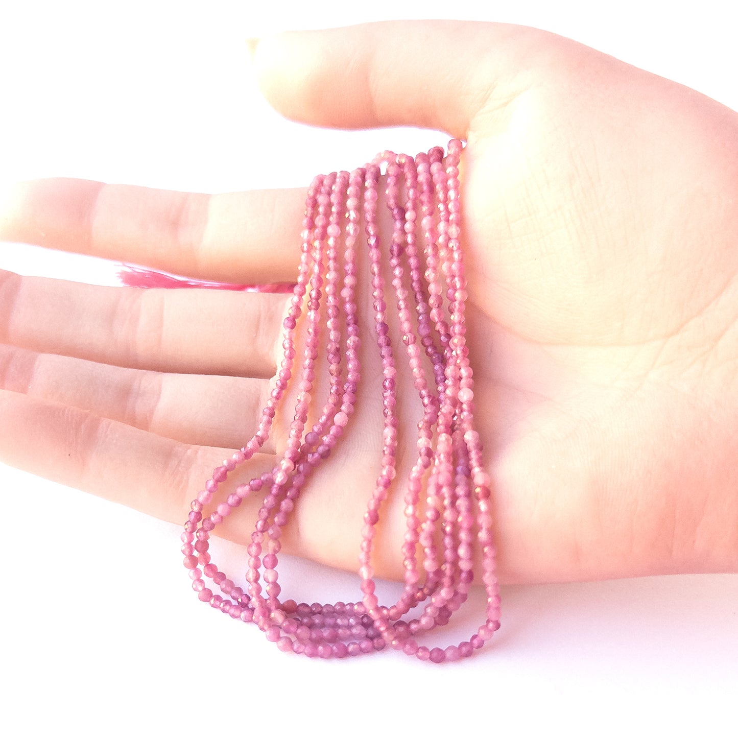 A person holds delicate strands of Pink Tourmaline beads, showcasing their faceted rondelle design.
