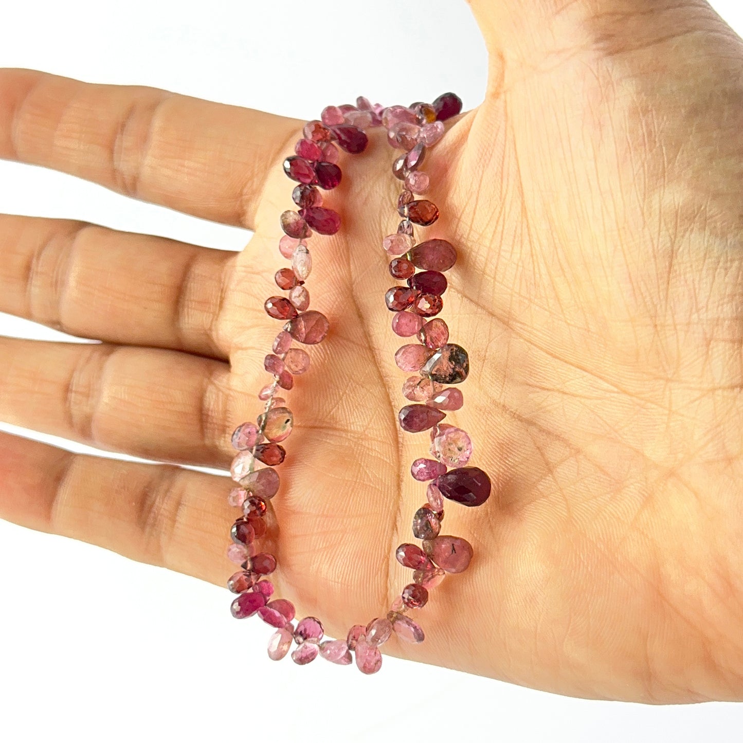 A person holds delicate strands of pink tourmaline beads, showcasing their faceted teardrop design
