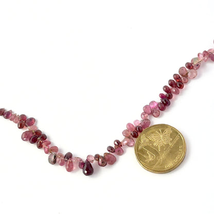 A coin is placed near delicate strands of pink tourmaline beads for scale.