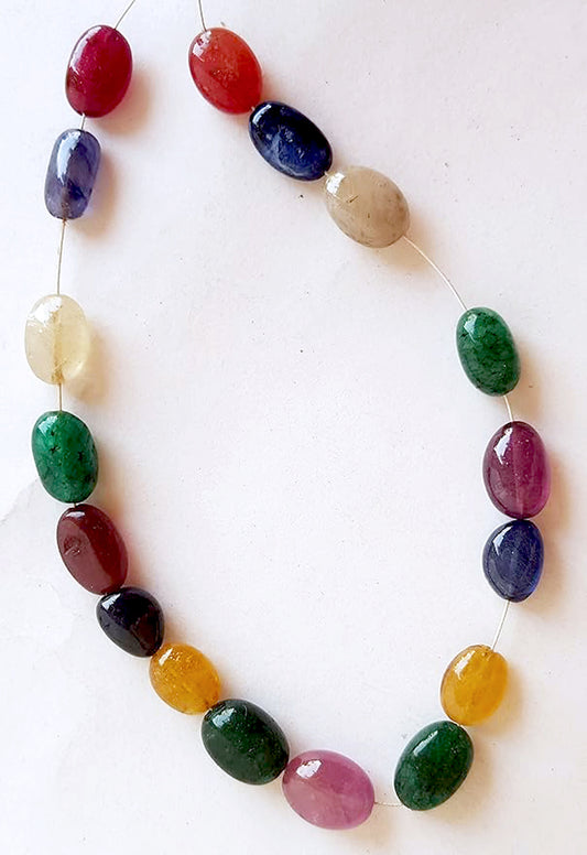 A colourful strand made of smooth oval, precious natural beads in ruby, blue sapphire, yellow sapphire, and emerald against a white backdrop.