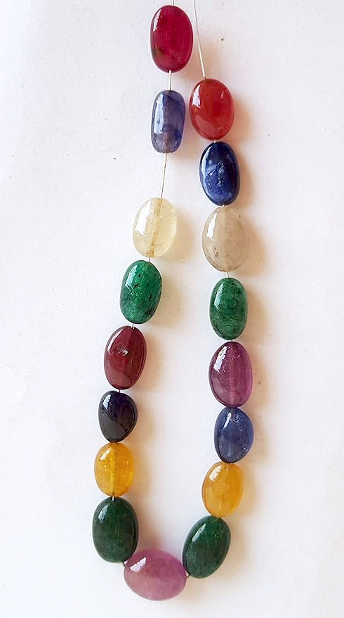   A vibrant multi-coloured strand featuring ruby, blue sapphire, yellow sapphire, and emerald beads on a white background.