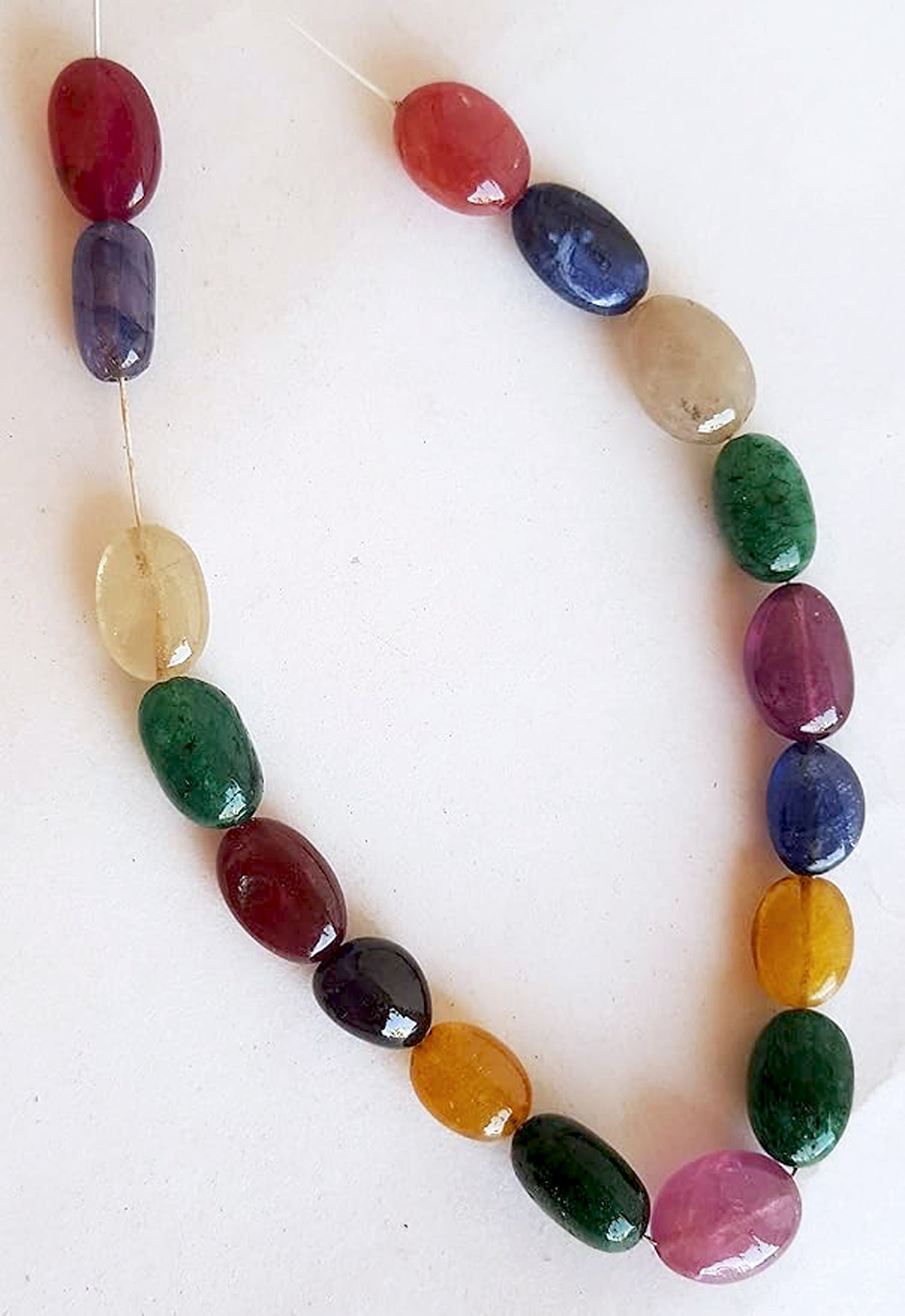  A striking strand with multi-coloured beads, including ruby, blue sapphire, yellow sapphire, and emerald, set on a white background.