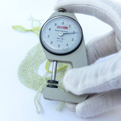 A dial gauge measures the Prehnite Faceted Rondelle 2.2mm gemstone.