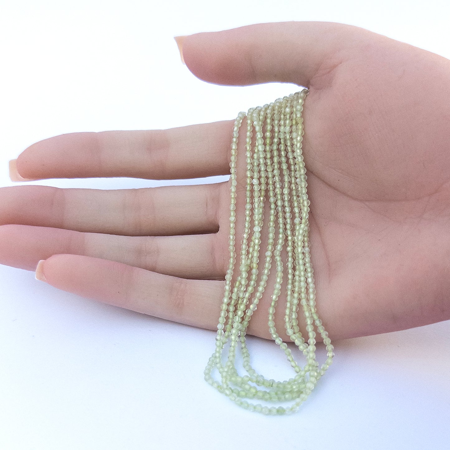 A person holds delicate strands of Prehnite beads, showcasing their Faceted Rondelle design.