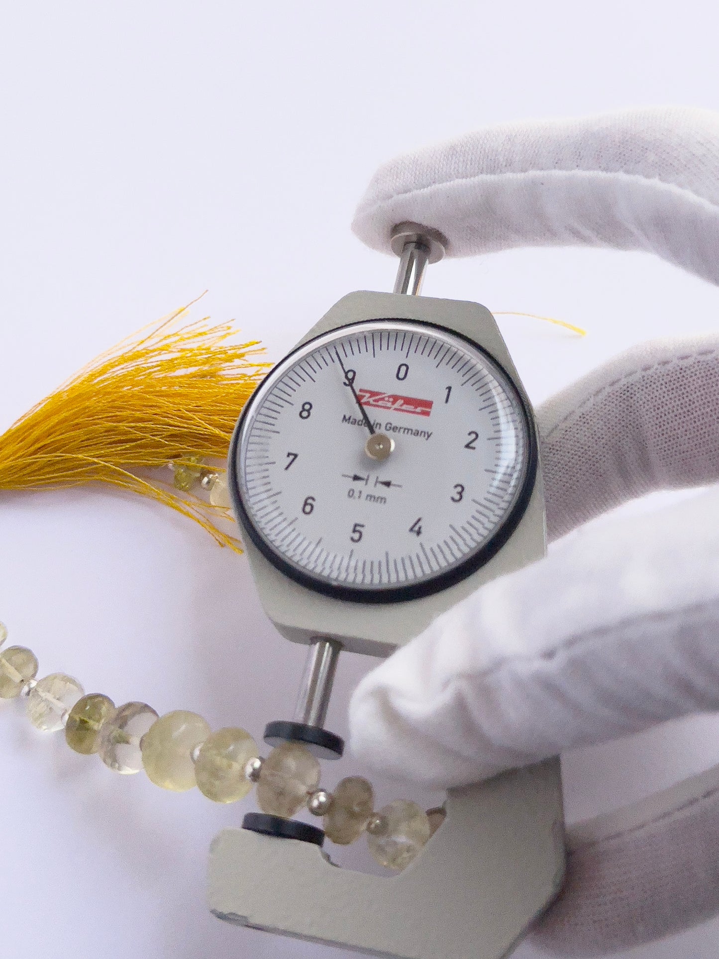 A dial gauge measures the Prehnite faceted rondelle 6.5–9mm gemstone.