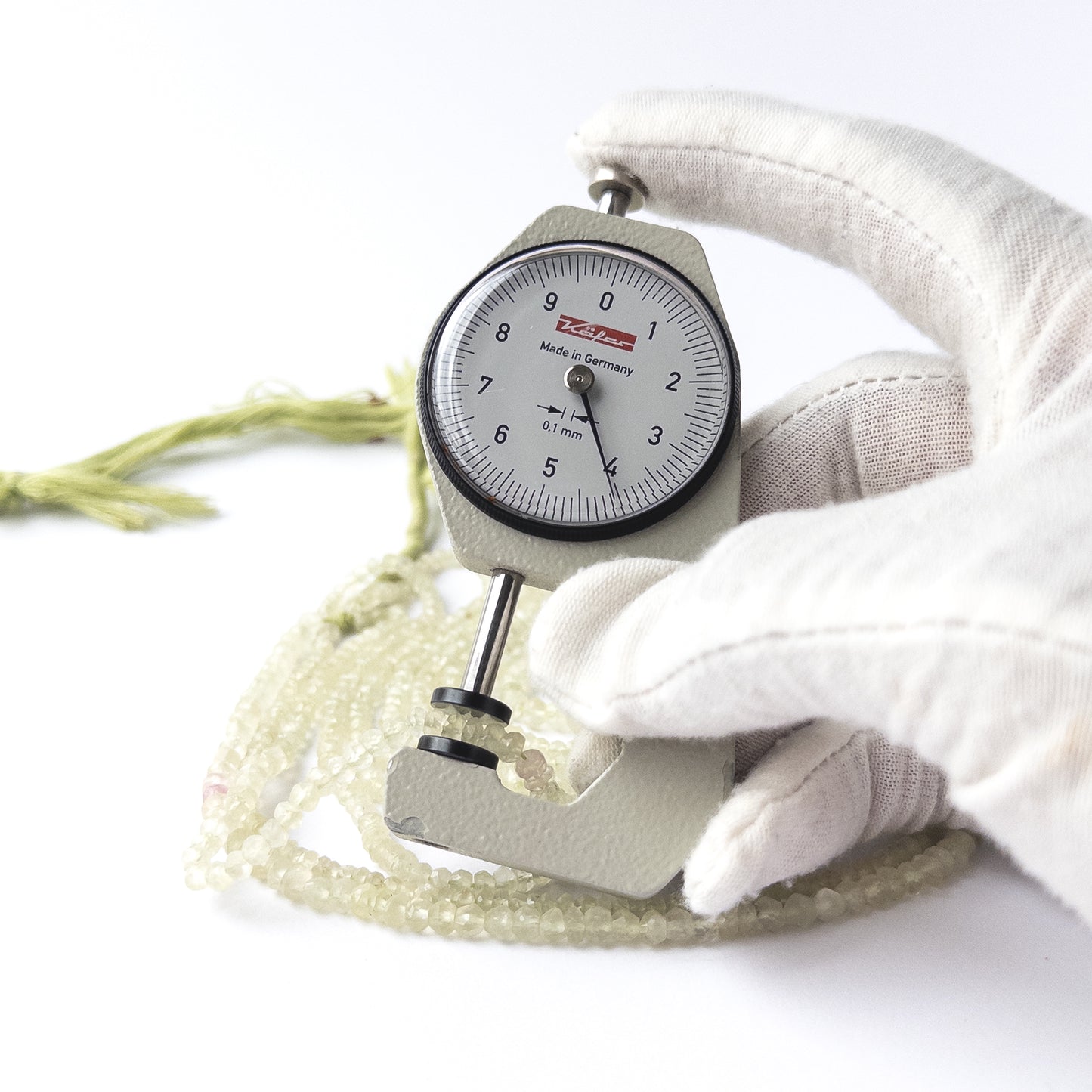 A dial gauge measures the Prehnite faceted rondelle 3.5–4.2mm bead size gemstone.