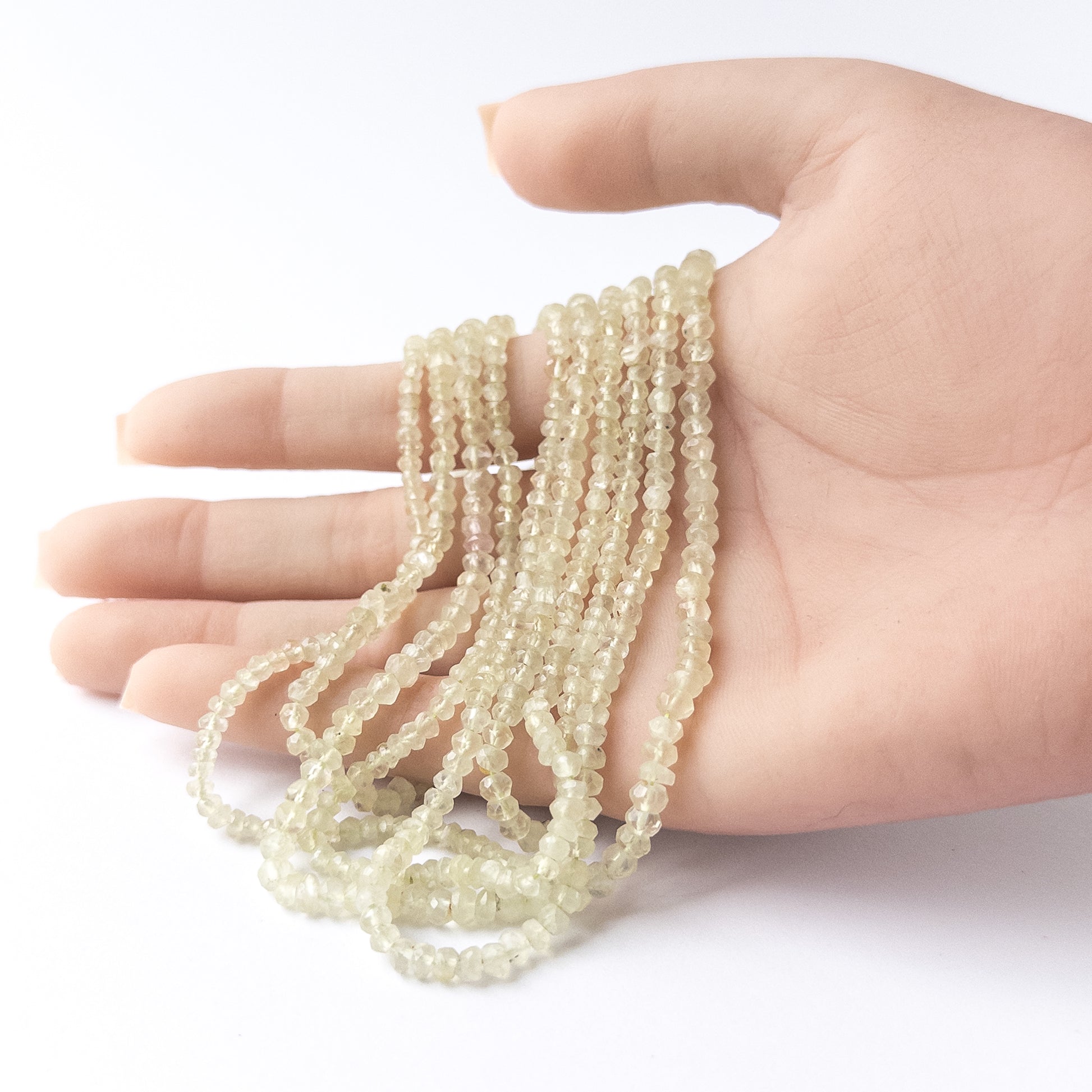 A person holds delicate strands of Prehnite beads, showcasing their faceted rondelle design.