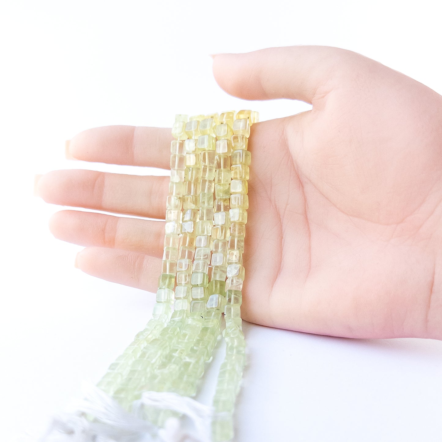 A person holds delicate strands of Prehnite beads, showcasing their smooth cube design.