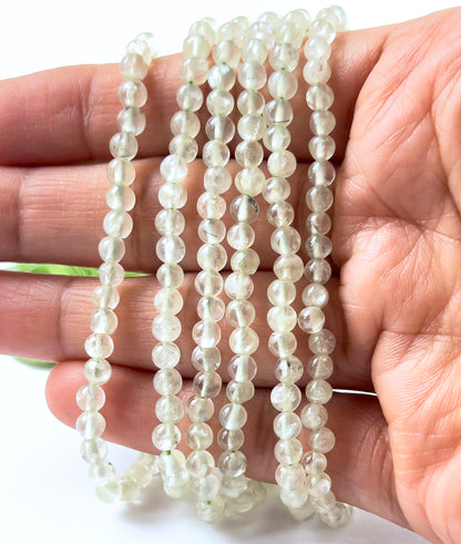 A person holds Prehnite smooth round beads, showing their spherical design and soft green colour.