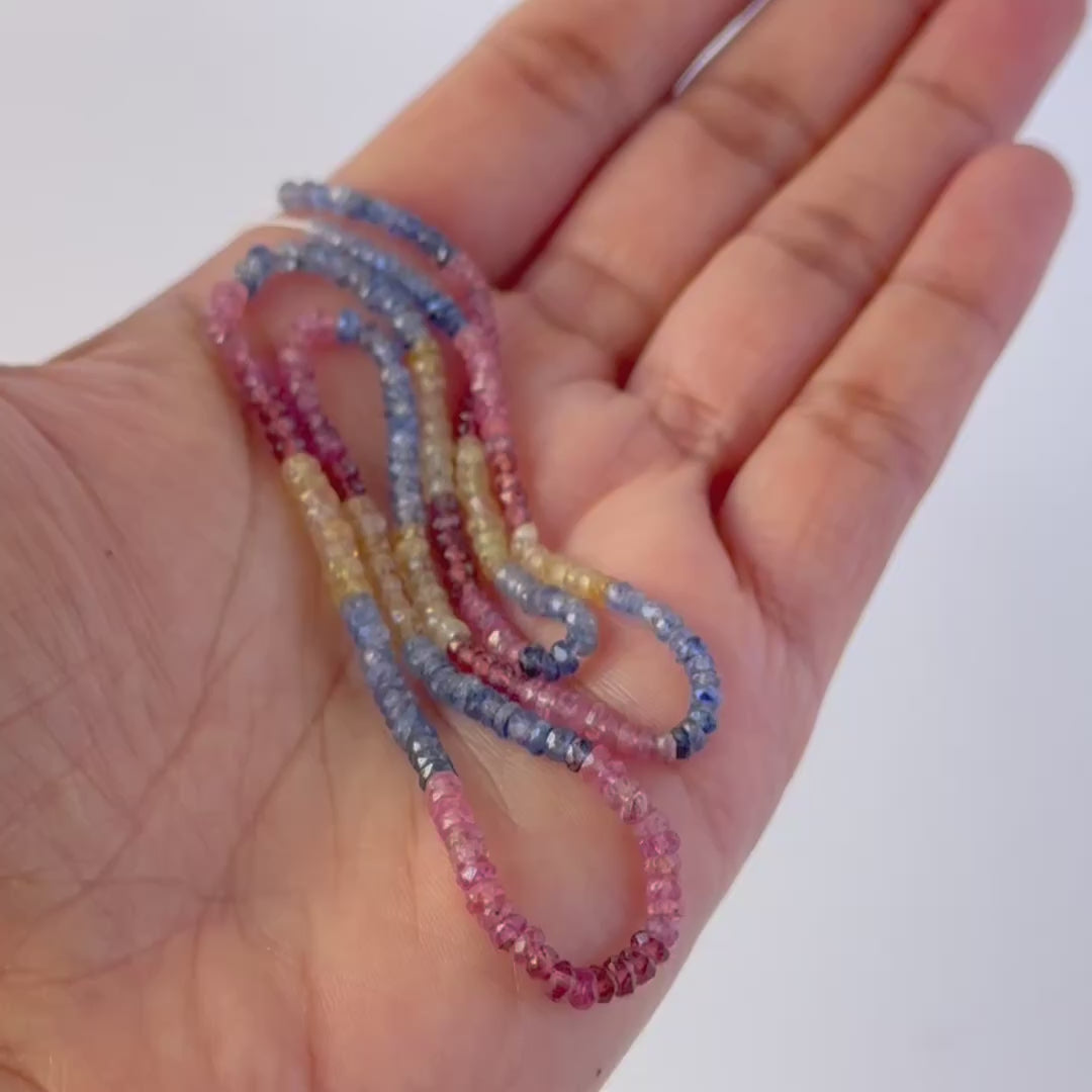 A person holds delicate strands of Multi Precious beads, showcasing their faceted rondelle design and sparkles.