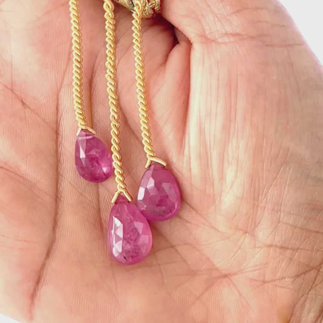 A person holds delicate strands of Ruby beads, showcasing their faceted teardrop design.