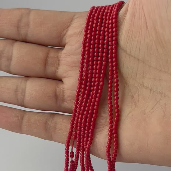 A person holds delicate strands of Taiwan Coral smooth round gemstone beads.