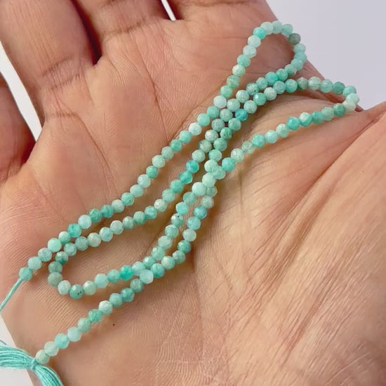 A video person holds delicate strands of Amazonite beads, showcasing their faceted rondelle design and sparkle.