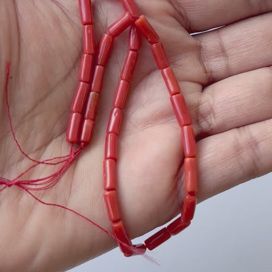 A person holding Smooth Italian Coral cylinder beads.