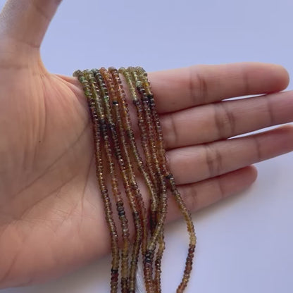 Hand holding stands of tourmaline 3-.3.5mm gemstone beads, as seen on Melbourne Gemstone Beads.