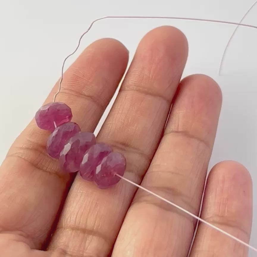 A video person holds Ruby beads, showcasing their faceted rondelle design and sparkle.