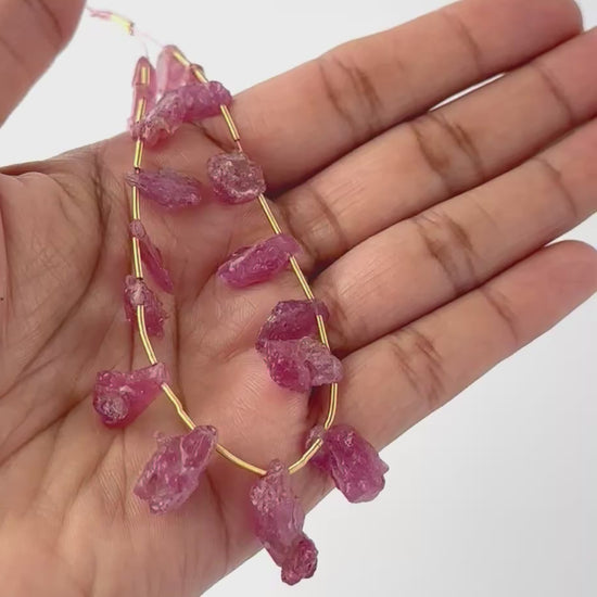 A video person holds delicate Ruby rough pieces, showcasing their side‑drilled design and sparkle.