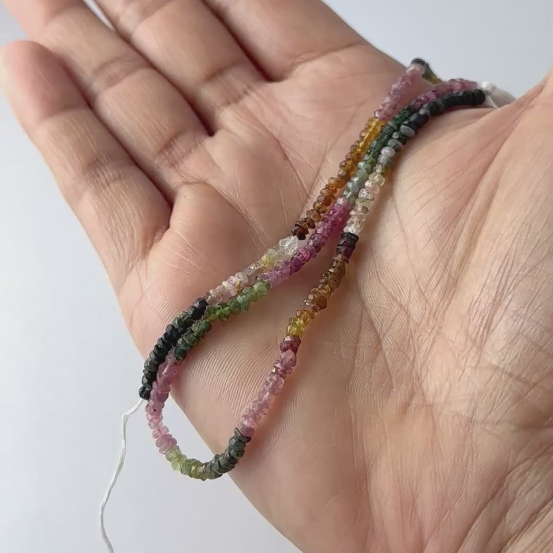 A video person holds delicate strands of Watermelon Tourmaline beads, showcasing their faceted rondelle design and sparkle.
