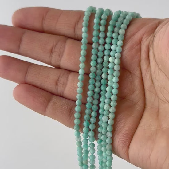 A video person holds delicate strands of Amazonite beads, showcasing their faceted rondelle design and sparkle.