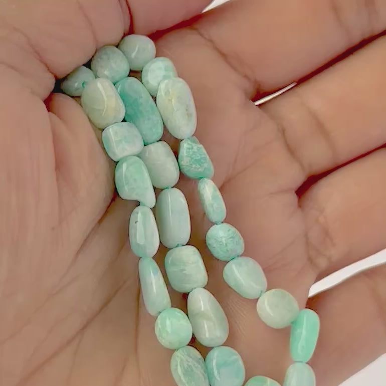 A video person holds delicate strands of Amazonite beads, showcasing their tumble‑smooth design and gentle shine.