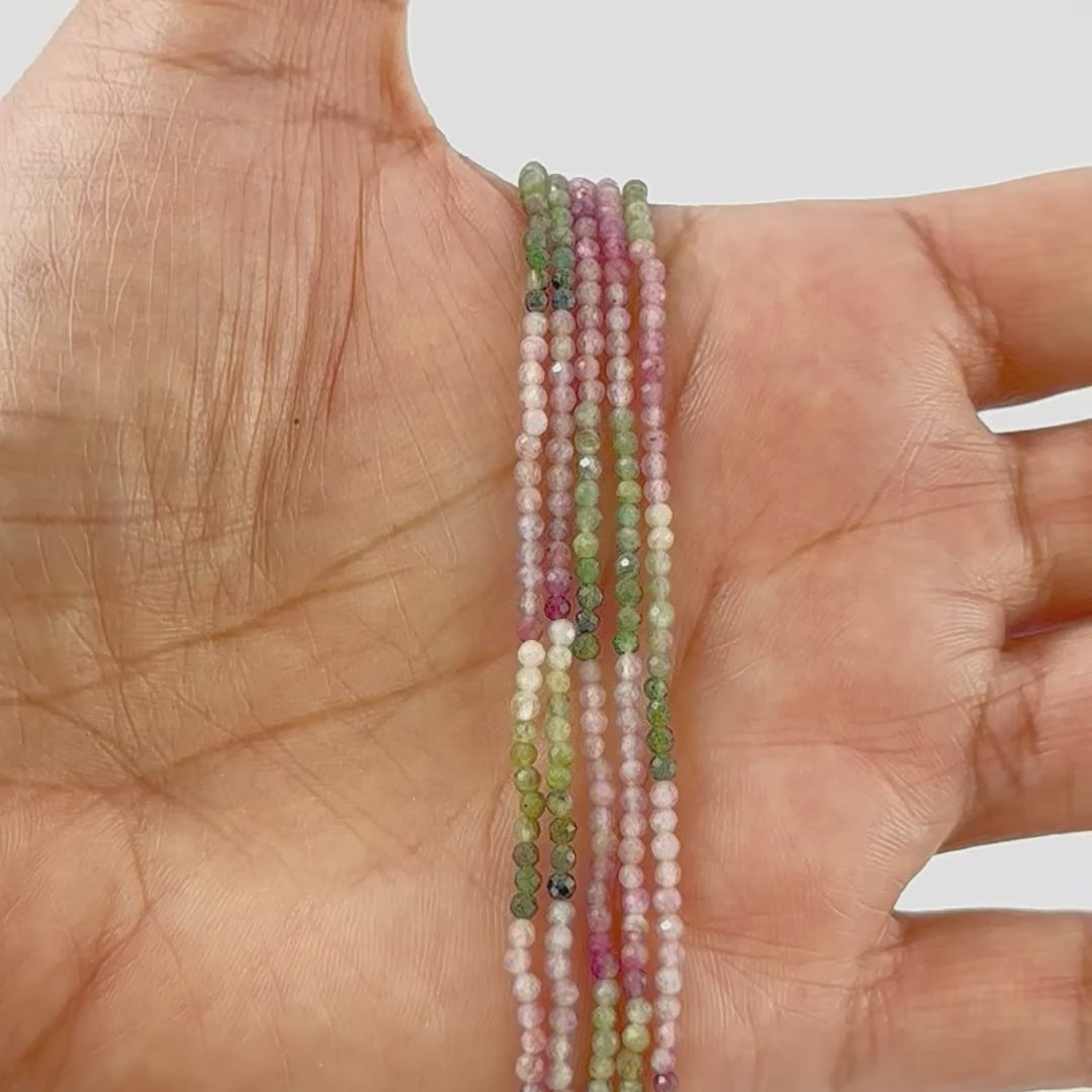 A person holds delicate strands of Tourmaline beads, showcasing their faceted rondelle design.