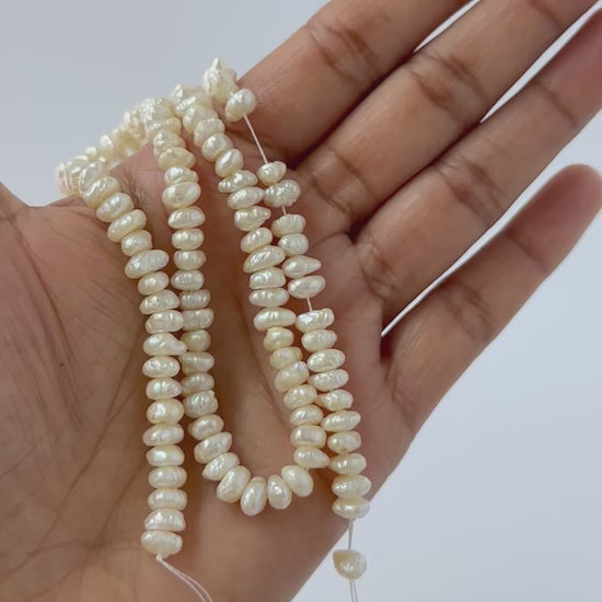 A person holds delicate strands of Freshwater Pearl beads, showcasing their smooth design.