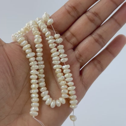 A person holds delicate strands of Freshwater Pearl beads, showcasing their smooth design.